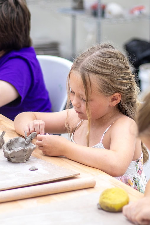 A young girl molds a piece of clay.